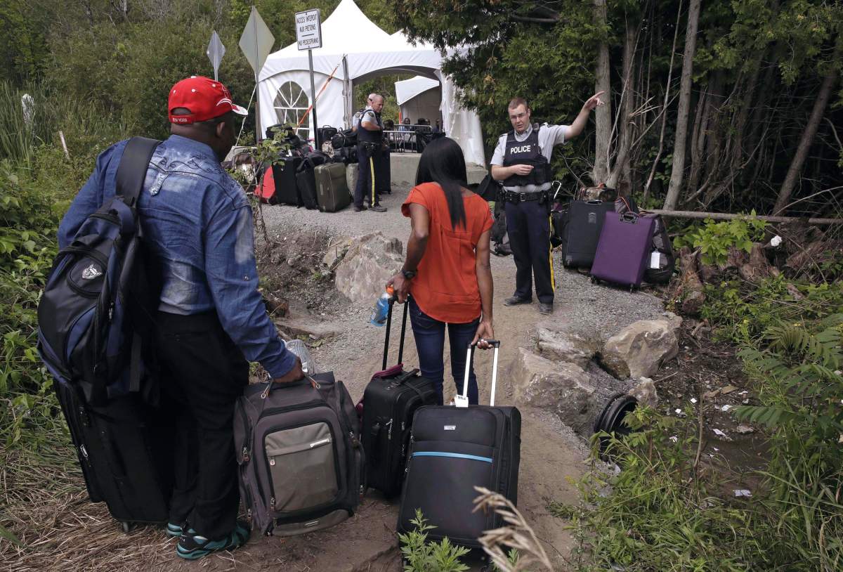 In this Aug. 7, 2017 file photo, an RCMP officer informs a migrant couple of the location of a legal border station, shortly before they illegally crossed from Champlain, N.Y., to Saint-Bernard-de-Lacolle, Quebec, using Roxham Road.