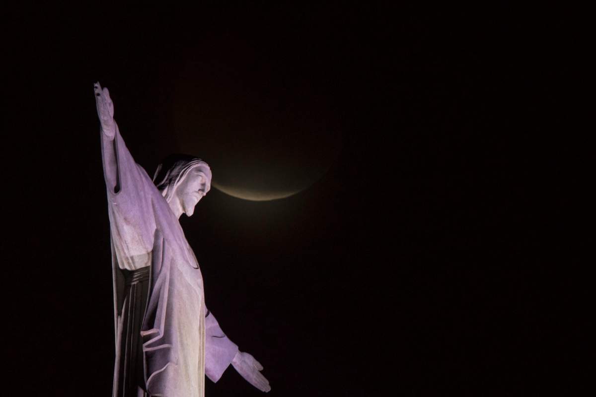 A blood moon rises above Christ the Redeemer statue during a lunar eclipse in Rio de Janeiro, Brazil, on Monday, Jan. 21, 2019.