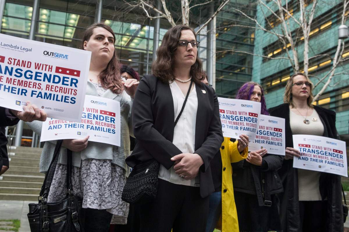 In this March 27, 2018 file photo, plaintiff U.S. Army Ssgt. Katie Schmid, center, listens to a speaker during a news conference following oral arguments in a case to block a transgender military ban at the U.S. Western District Federal Courthouse in Seattle.