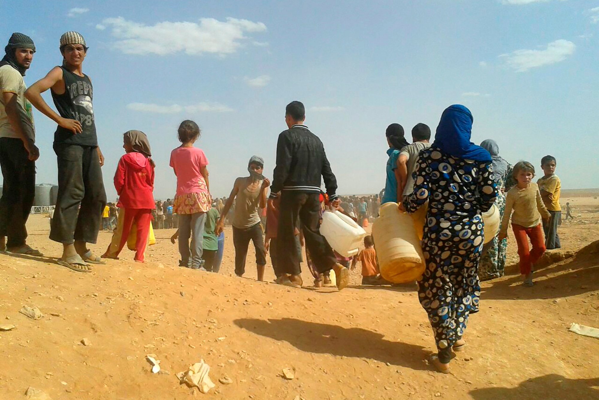In this June 23, 2016 file photo, Syrian refugees gather for water at the informal Rukban camp for displaced Syrians, between the Jordan and Syria borders.