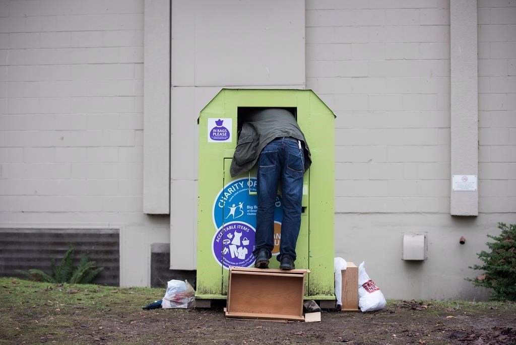 A man tries to retrieve items from a clothing donation bin in Vancouver on Wednesday, Dec. 12, 2018.