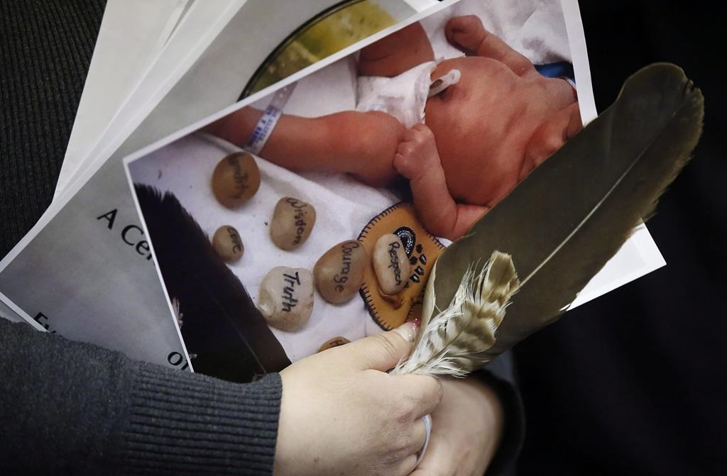 A woman holds a photo of a baby and an eagle feather at a press conference in support of the mother who's newborn baby was seized from hospital by Manitoba's Child and Family Services (CFS) at First Nations Family Advocate Office in Winnipeg on January 11, 2019.