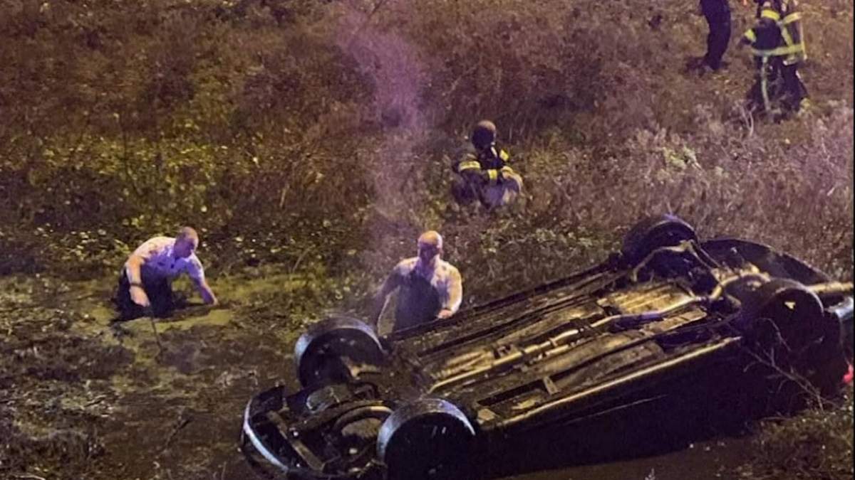 First responders tread through muddy waters surrounding the overturned car.