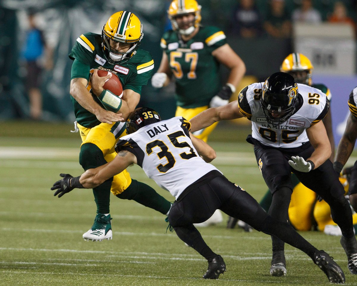 Hamilton Tiger-Cats Mike Daly (35) and Julian Howsare (95) try to tackle Edmonton Eskimos quarterback Mike Reilly (13) during second half CFL action in Edmonton, Alta., on Friday June 22, 2018. 