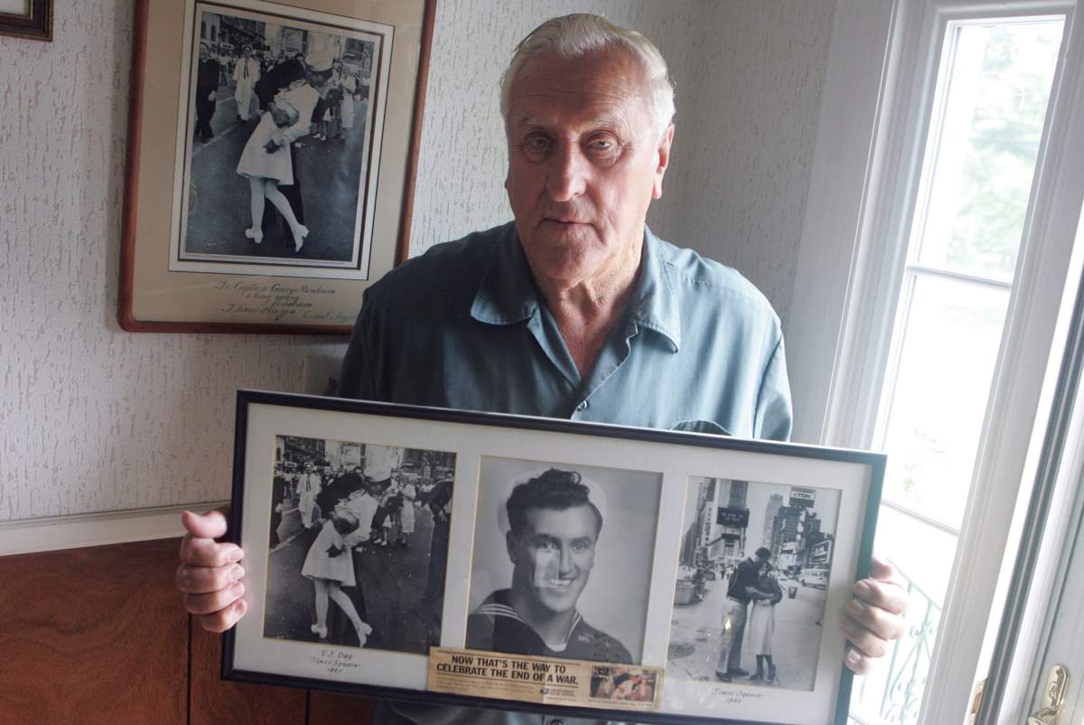 In this July 2, 2009, photo George Mendonsa poses for a photo in Middletown, R.I., holding a copy of the famous Alfred Eisenstadt photo of Mendonsa kissing a woman in a nurse’s uniform in Times Square on Aug. 14, 1945, while celebrating the end of World War II, left.