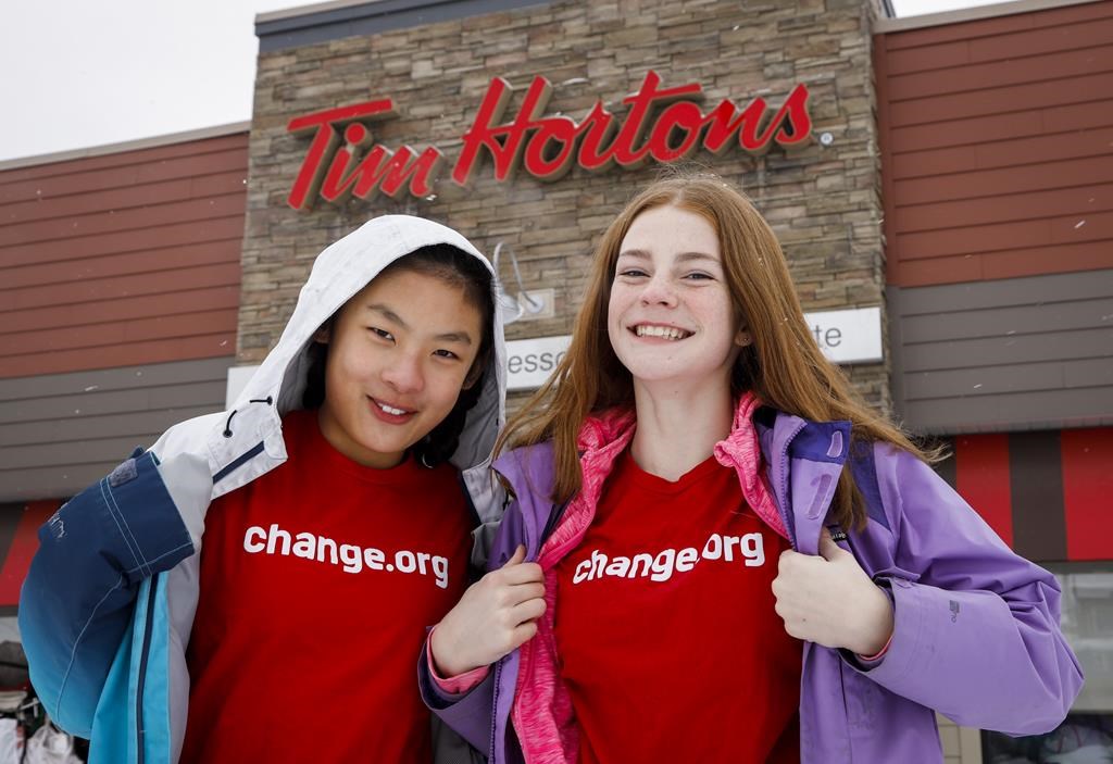 Mya Chau, left, 12, and Eve Helman, 12, who are digitally petitioning Tim Hortons to make the Roll up the Rim to Win campaign more environmentally friendly, are seen outside a Tim Hortons in Calgary, Alta., Sunday, Feb. 3, 2019.