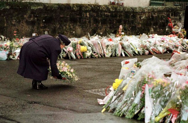 In this March 17, 1996, file photo, Britain’s Queen Elizabeth places a floral bouquet with hundreds of others in front of Dunblane Primary School.