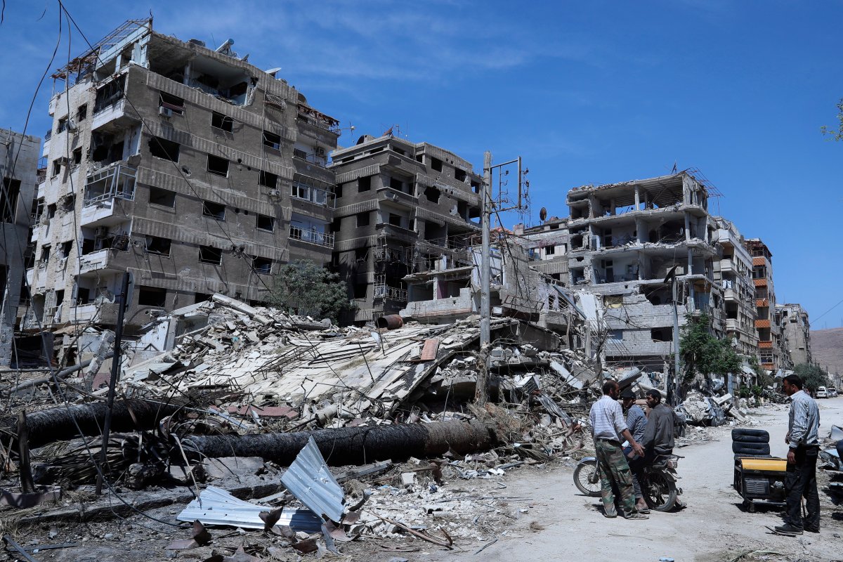 FILE - In this Monday, April 16, 2018 file photo, people stand in front of damaged buildings, in the town of Douma, the site of a suspected chemical weapons attack, near Damascus, Syria.