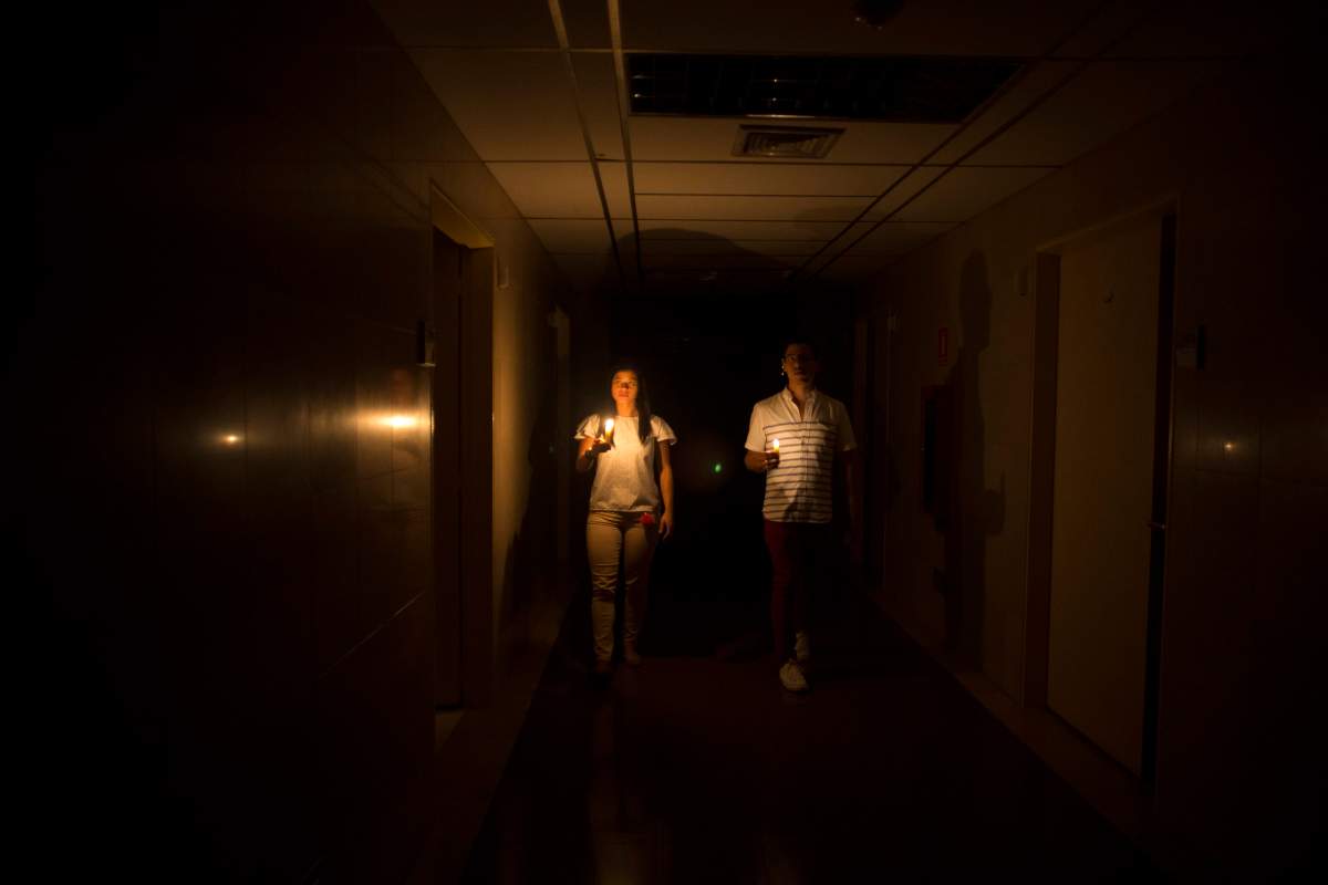 Relatives of a patient walk in the darkened hall of a clinic with a candle lighting the way, during a power outage in Caracas, Venezuela, Thursday, March 7, 2019.