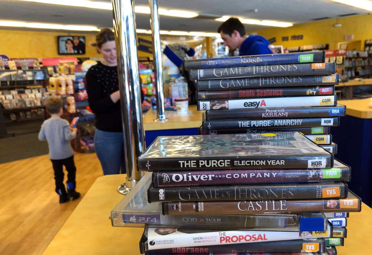 Returned movies wait to be shelved at the last Blockbuster on the planet in Bend, Ore., on Monday, March 11, 2019, as a customer checks out movies in the background.