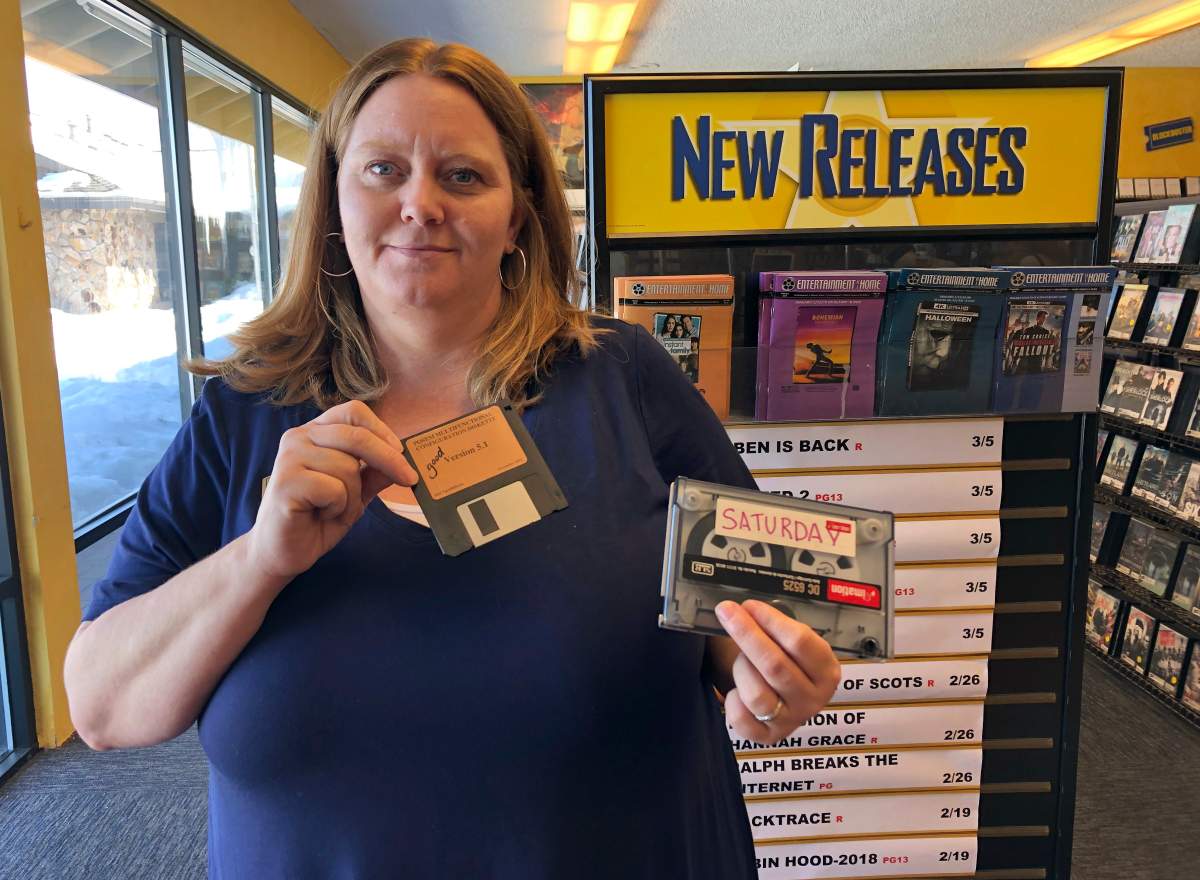 Sandi Harding, general manager of the last Blockbuster on the planet in Bend, Ore., poses for a photo inside the store on Monday, March 11, 2019. Harding is holding up the floppy disc she uses to reboot her computer and the reel-to-reel tape used to back up transactions.