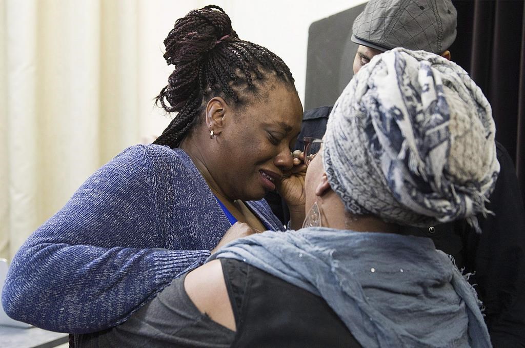 Johanne Coriolan, left, a family member of Pierre Coriolan, is consoled by activsts Wil Prosper and Maguy Metellus following a news conference in Montreal, Wednesday, February 7, 2018.