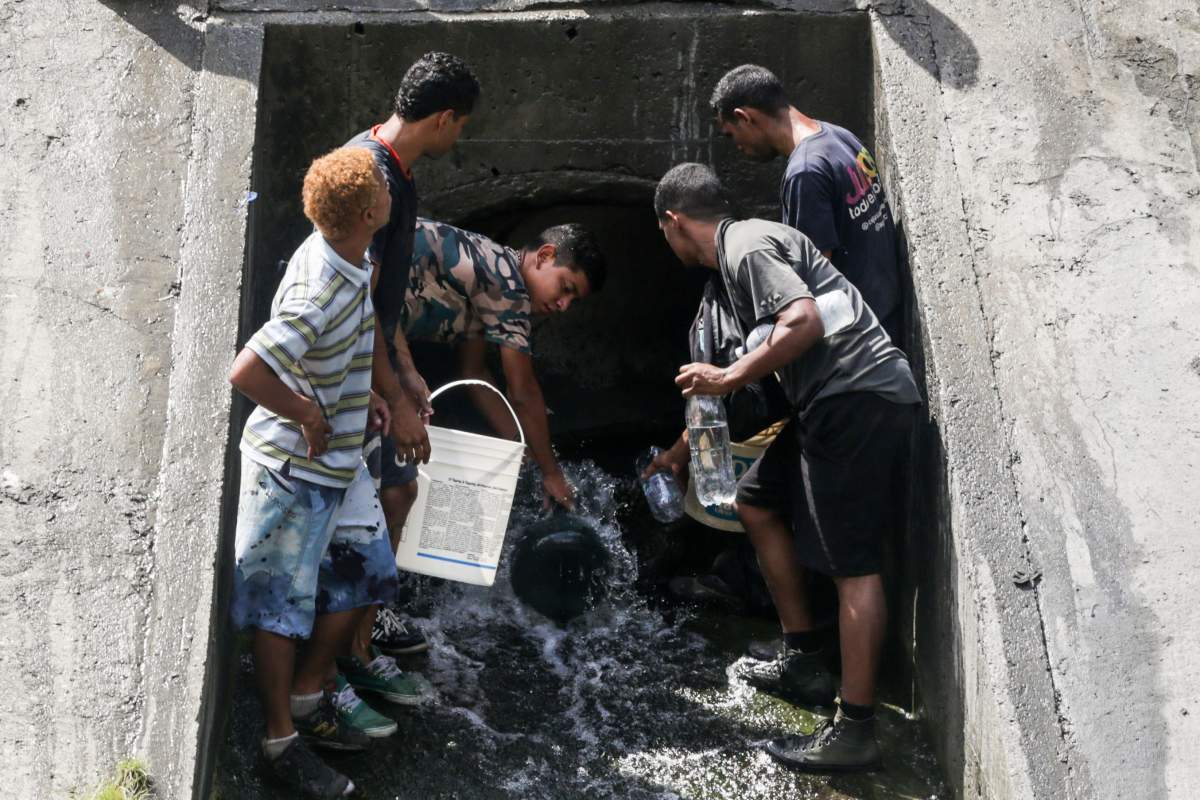 People collect water from a sewage canal at the river Guaire in Caracas on March 11, 2019, as a massive power outage continues affecting some areas of the country.