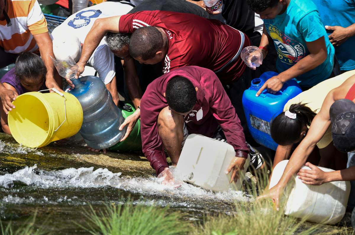 People collect water from a sewage canal at the river Guaire in Caracas on March 11, 2019, as a massive power outage continues affecting some areas of the country.