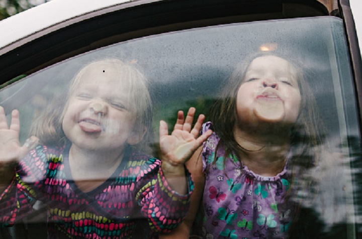 Playful sisters making faces while traveling in car seen through window.