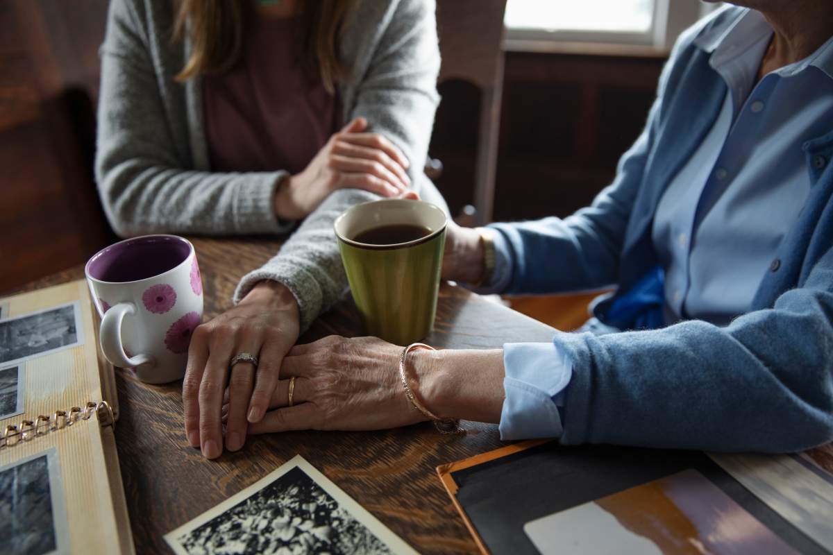 A file photo of an affectionate senior mother and daughter holding hands, drinking coffee and looking at photo albums.