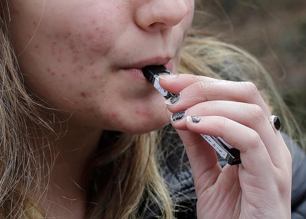 FILE - In this April 11, 2018, file photo, a high school student uses a vaping device near a school campus in Cambridge, Mass. U.S. health regulators are moving ahead with a plan to keep e-cigarettes out of the hands of teenagers by restricting sales of most flavored products in convenience stores and online. (AP Photo/Steven Senne, File).
