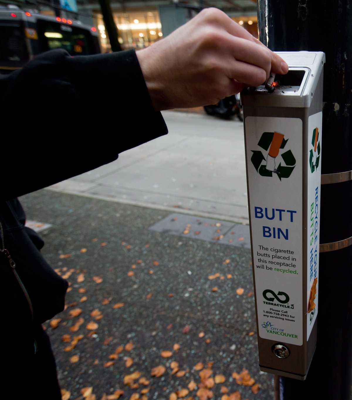 Photo of a smoker discarding a cigarette butt into a recycling bin.