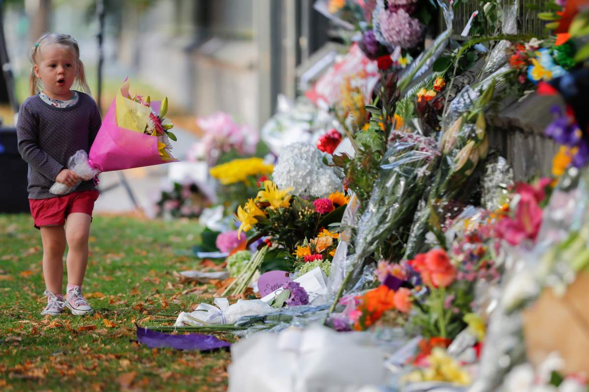 In this March 17, 2019, file photo, a girl carries flowers to a memorial wall following the mosque shootings in Christchurch, New Zealand. 