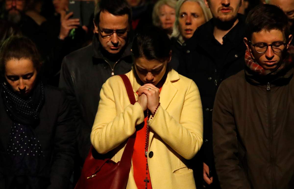 People pray as Notre Dame Cathedral burns in Paris, Monday, April 15, 2019.