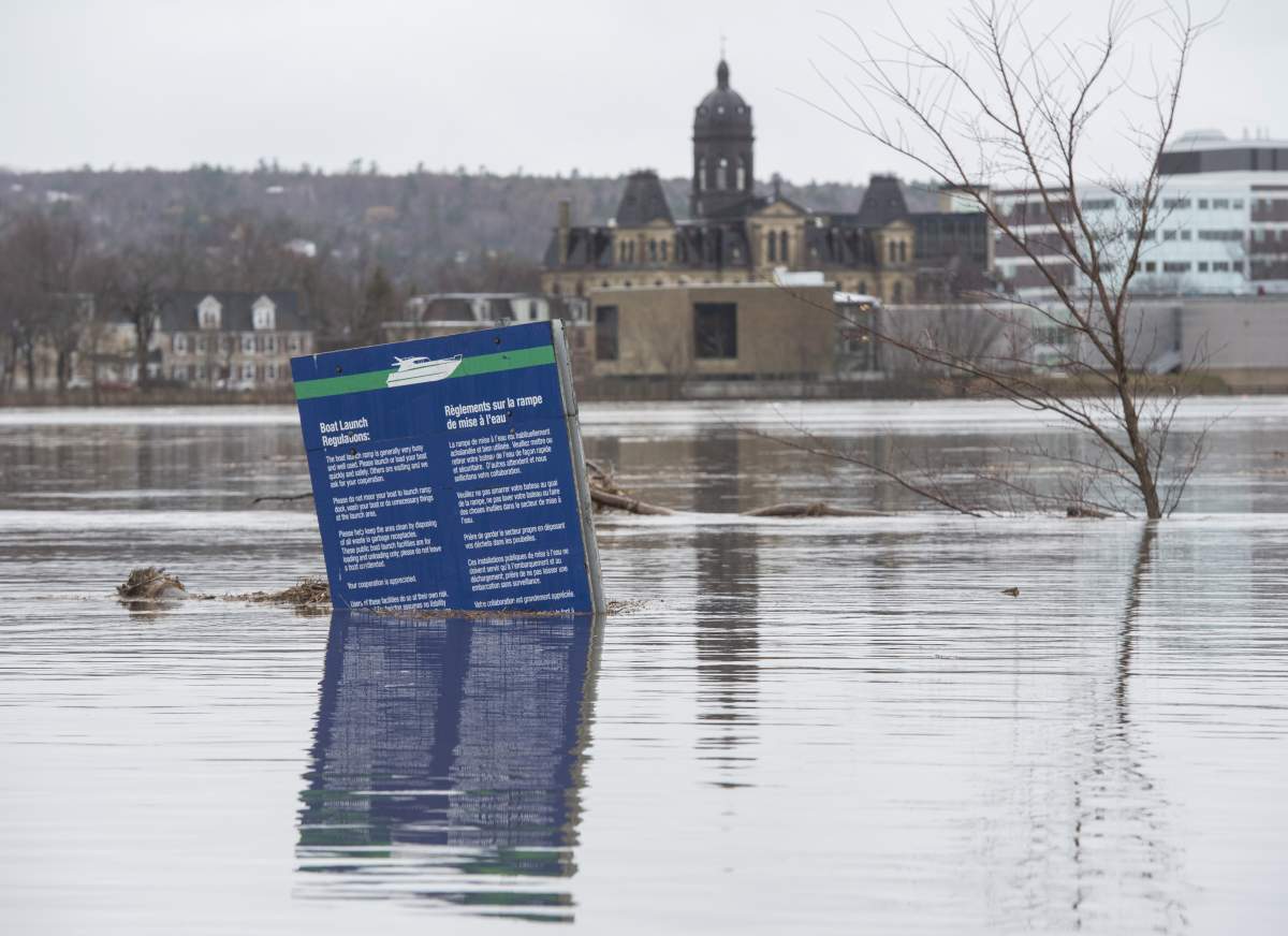 The New Brunswick Legislature is seen in the background of a boat ramp sign in Carleton Park surrounded by the flood water and debris from the St. John River in Fredericton, N.B. on Saturday, April 20, 2019. THE CANADIAN PRESS/Stephen MacGillivray