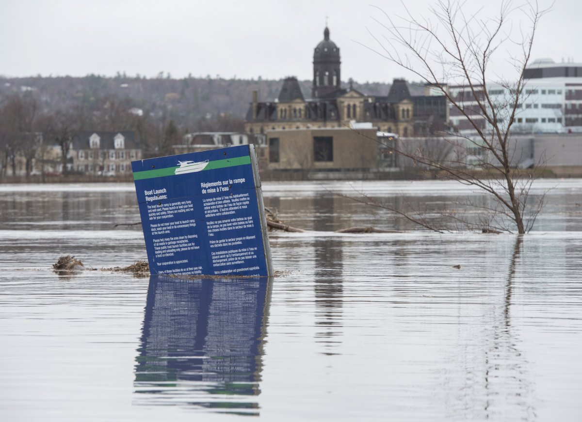 The New Brunswick Legislature is seen in the background of a boat ramp sign in Carleton Park surrounded by the flood water and debris from the St. John River in Fredericton, N.B. on Saturday, April 20, 2019.