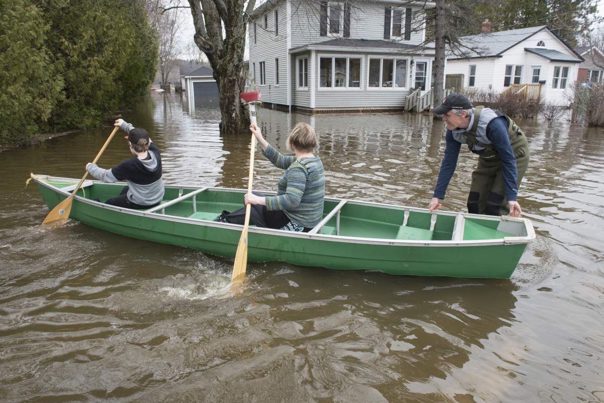 Peter Toner, right, Peta Fussell and their son Harry, 11, use a canoe and chest waders to check on their home on Riverside Drive in Fredericton on Monday April 22, 2019.