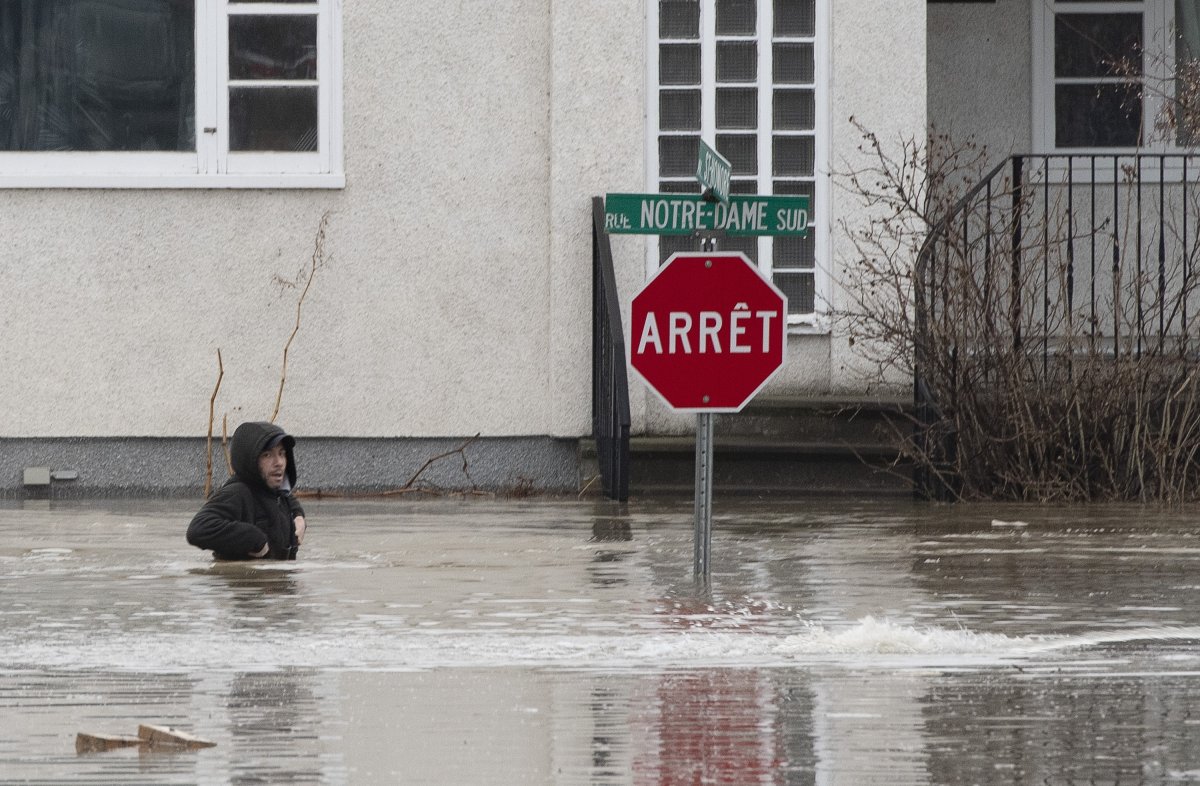 A man hops in the water of a flooded street to get to a house on Saturday, April 20, 2019 in Ste-Marie Que.