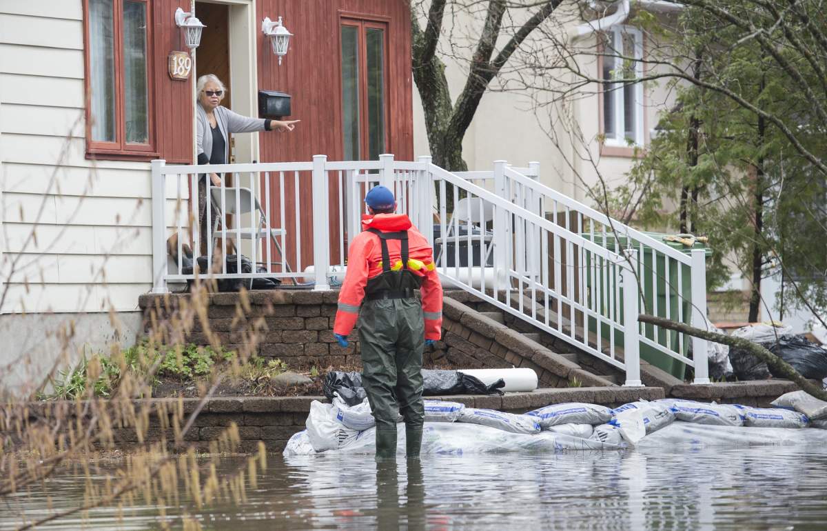 A woman talks to a volunteer emergency worker at her home on a residential street surrounded by floodwaters on Île-Bizard west of Montreal, Saturday, April 27, 2019.