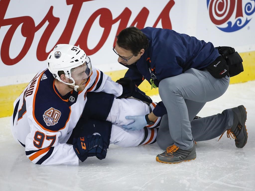 Edmonton Oilers' Connor McDavid, left, has his knee tended too after crashing into Calgary Flames goalie Mike Smith during second period NHL hockey action in Calgary, Saturday, April 6, 2019. McDavid will begin rehabilitating his leg immediately, the Edmonton Oilers announced late Friday. THE CANADIAN PRESS/Jeff McIntosh.