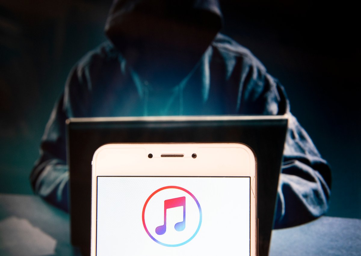 iTunes logo is seen on an Android mobile device with a figure of hacker in the background.