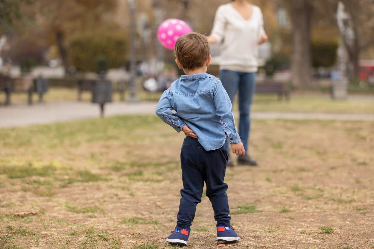 Toddler scratching back with a hand while playing in the park. 