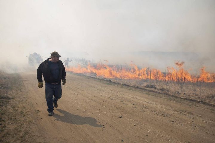 An onlooker walks past a brush fire near Biggar, Sask., on Tuesday, April 23, 2019.