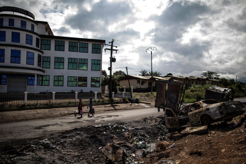 Women pass by the edge of the abandoned market into the majority anglophone South West province in Buea, on October 3, 2018 next the wreckage of a car burned allegedly by separatists fighter in a recent attack. - The southwest, along with the northwest, has been torn by two-years of clashes between English-speaking fighters, who want to break away from majority francophone Cameroon, and government forces. 