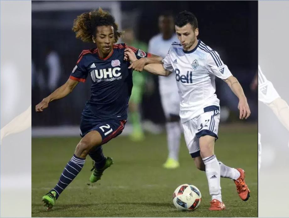 New England Revolution midfielder Zachary Herivaux (21) and Vancouver Whitecaps midfielder Marco Bustos vie for possession during an MLS preseason soccer game in  2016.