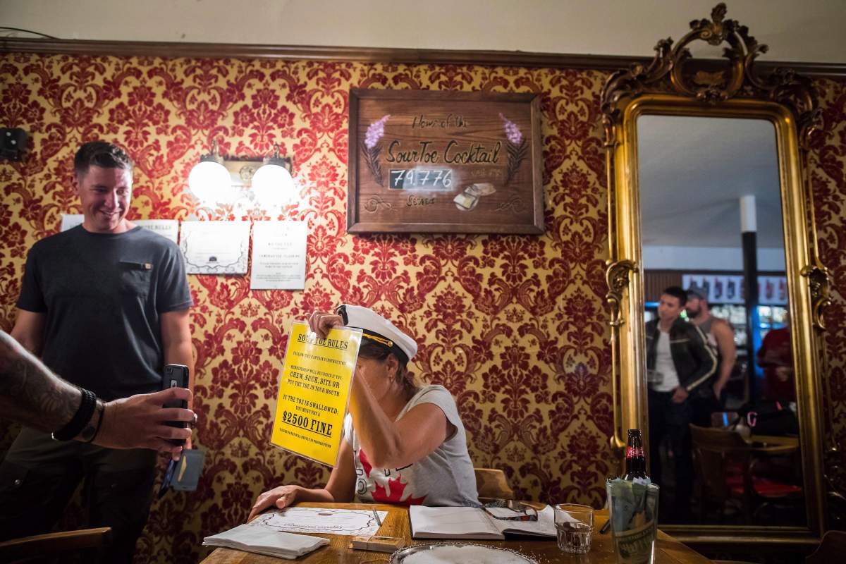 "Toe Captain" Sue Taylor holds up a list of rules while administering the drinking of the Sourtoe Cocktail, a drink containing a dehydrated human toe, in Dawson City, Yukon, on Sunday, July 1, 2018. 