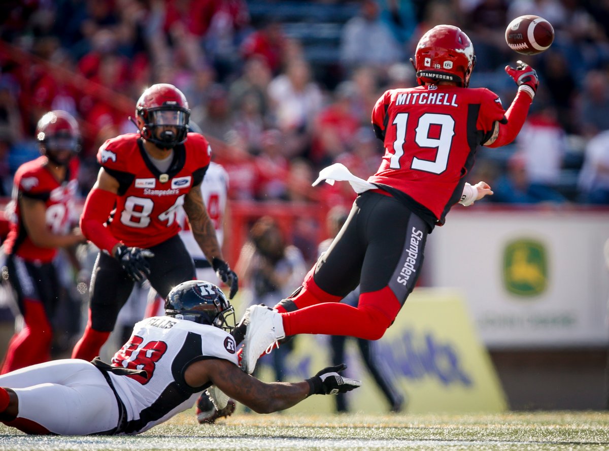 Ottawa Redblacks' Avery Ellis, left, grabs Calgary Stampeders quarterback Bo Levi Mitchell, as he throws the ball to Reggie Begelton, centre, during second-half CFL football action in Calgary, Saturday, June 15, 2019.