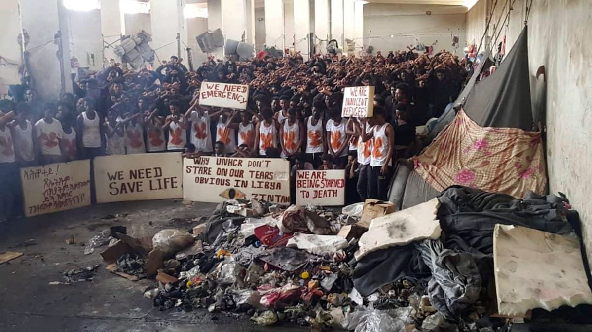 In this May 21, 2019 photo provided by an African migrant, hundreds of migrants stage a protest in a detention center in the town of Zintan, western Libya, appealing for help from the United Nations. 