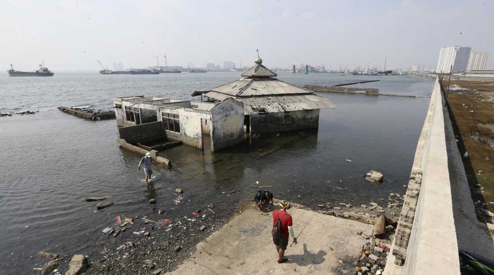 People walk near a giant sea wall which is used as a barrier to prevent sea water from flowing into land and cause flooding in Jakarta, Indonesia, Saturday, July 27, 2019.
