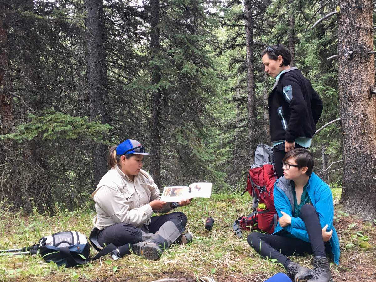 Diandra Bruised Head reads from a bison book as Kansie Fox and her daughter, Monroe, listen in the backcountry of Banff National Park on July 3, 2019.