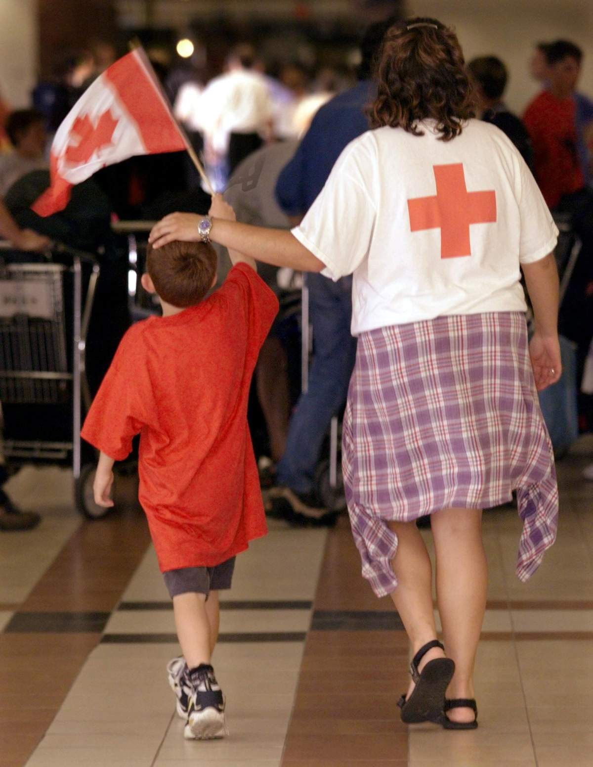 Kosovar refugee Mohammed Xhemajli, left, escorted by Red Cross worker Nicole Gillis, carries his Canadian flag through the airport in Halifax on Wednesday July 7, 1999 as he prepares to board an aircraft to return home.