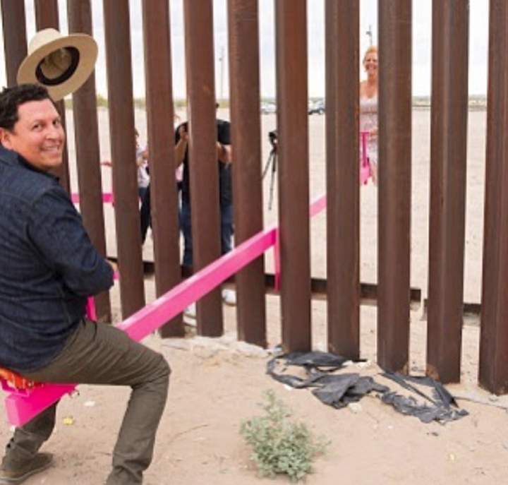 Ronald Rael, left, and his wife Virginia San Fratello are shown riding a seesaw set up at the U.S.-Mexico border on July 29, 2019.