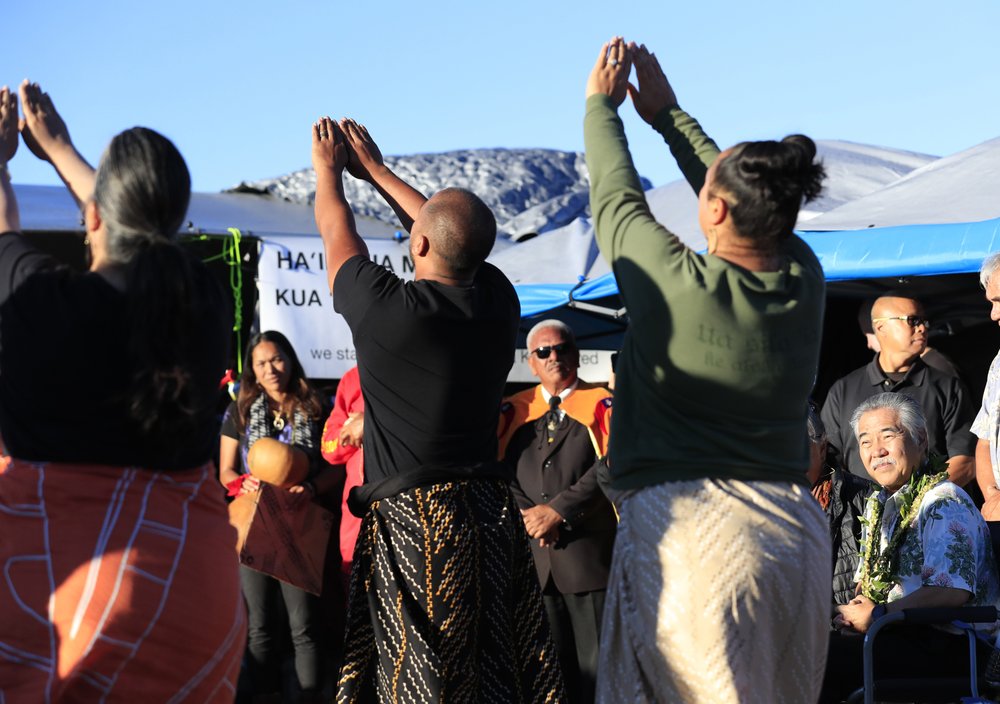 FILE - In this July 23, 2019, file photo, Hawaii governor David Ige, right, watches a kahiko hula performance during a visit to the ninth day of protests against the Thirty Meter Telescope at the base of Mauna Kea on Hawaii Island. Astronomers across 11 observatories on Hawaii’s tallest mountain have cancelled more than 2,000 hours of telescope viewing over the past four weeks because a protest blocked a road to the summit.