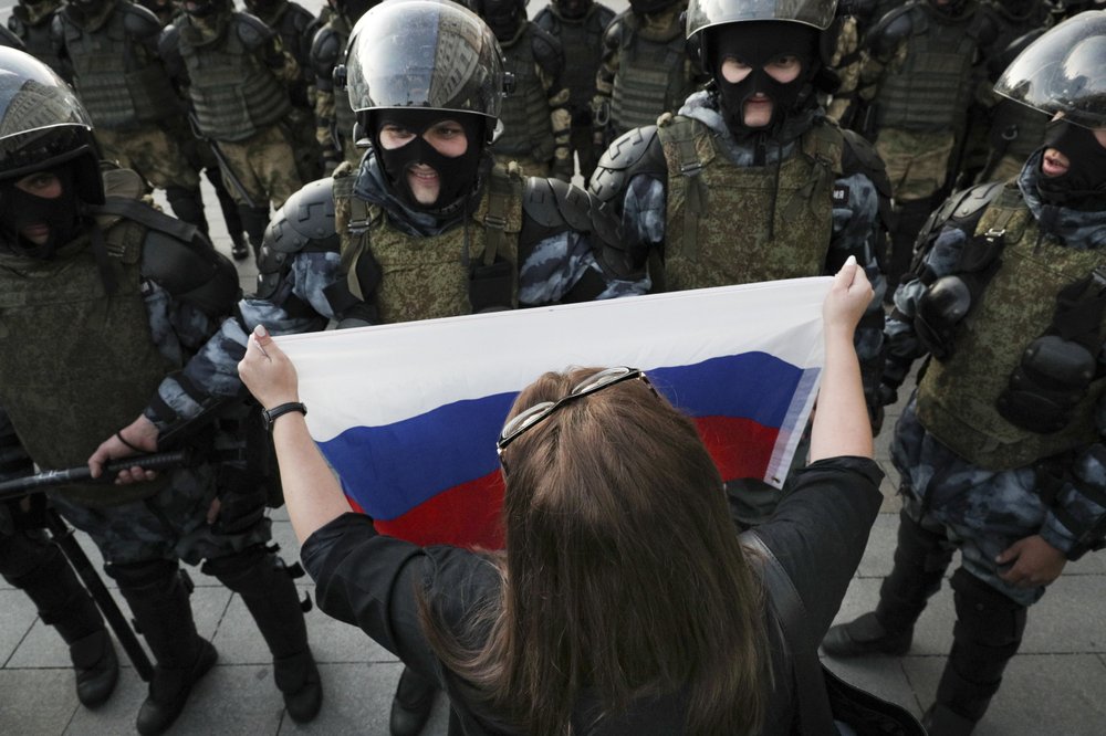 A woman holds a Russian national flag in front of police during a protest in Moscow, Russia, Saturday, Aug. 10, 2019. some thousands of people rallied in central Moscow for the third consecutive weekend to protest the exclusion of opposition and independent candidates from the Russian capital's city council ballot. 