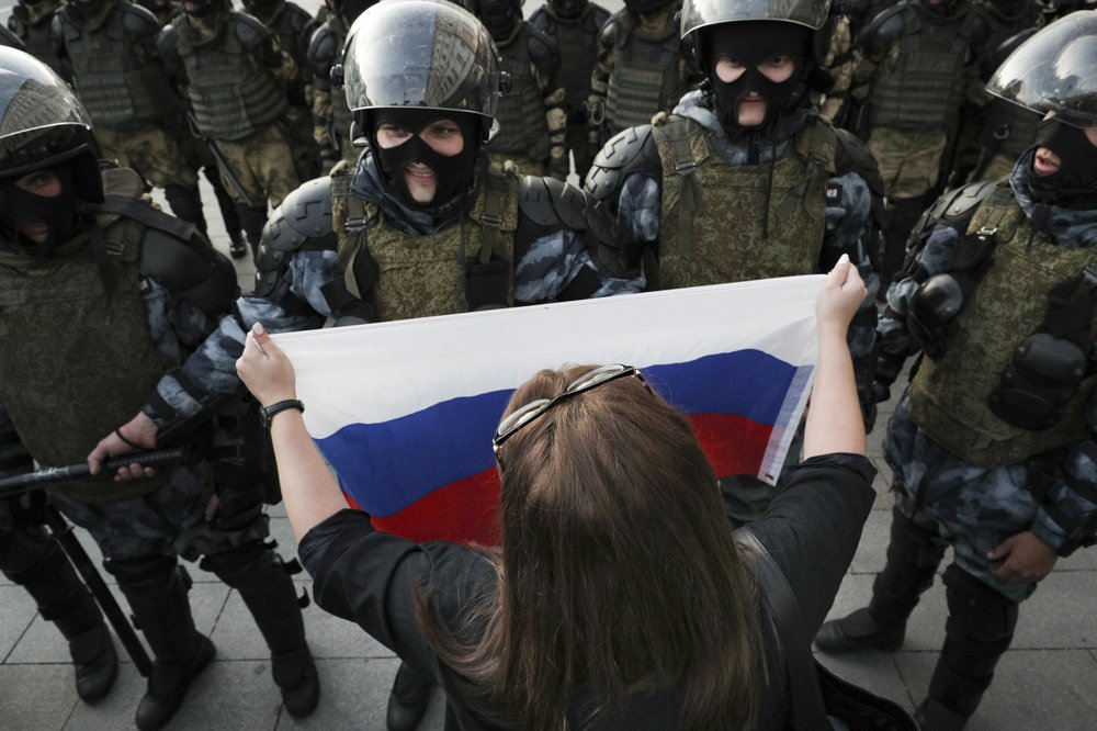 A woman holds a Russian national flag in front of police during a protest in Moscow, Russia, Saturday, Aug. 10, 2019. some thousands of people rallied in central Moscow for the third consecutive weekend to protest the exclusion of opposition and independent candidates from the Russian capital's city council ballot. 