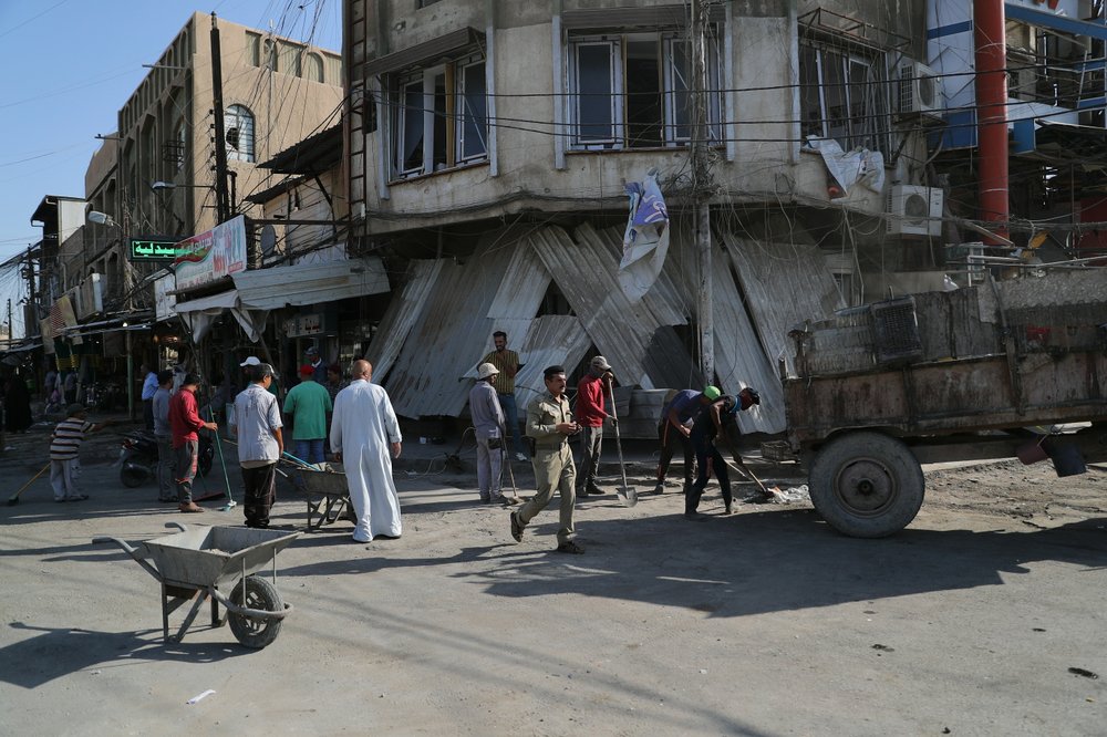 Municipality workers clean up as civilians inspect the aftermath a day after a motorcycle rigged with explosives exploded in Mussayyib, south of Baghdad, Iraq, Saturday, Aug. 24, 2019. The officials said Saturday that the blast occurred the previous evening on a commercial street in the village of Mussayyib, killing and wounding civilians.
