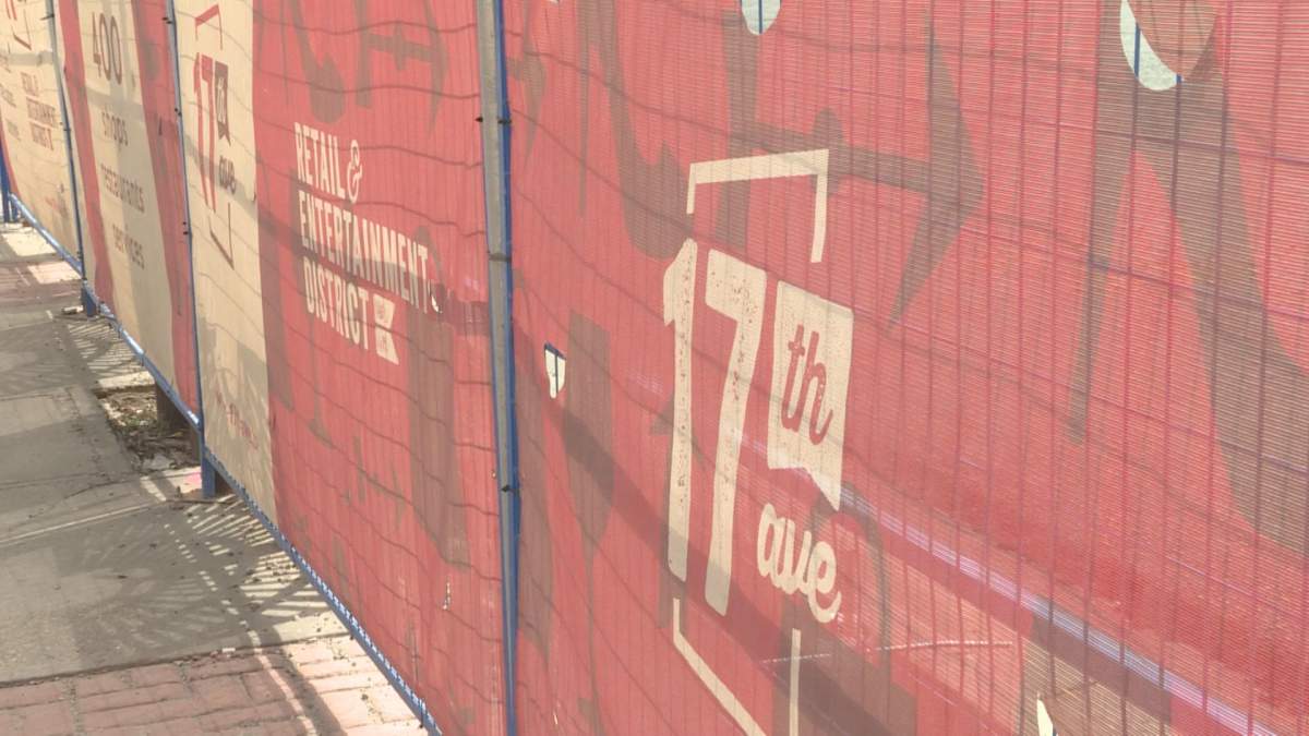 A construction security fence and shroud is shown along Calgary's 17 Avenue S.W.