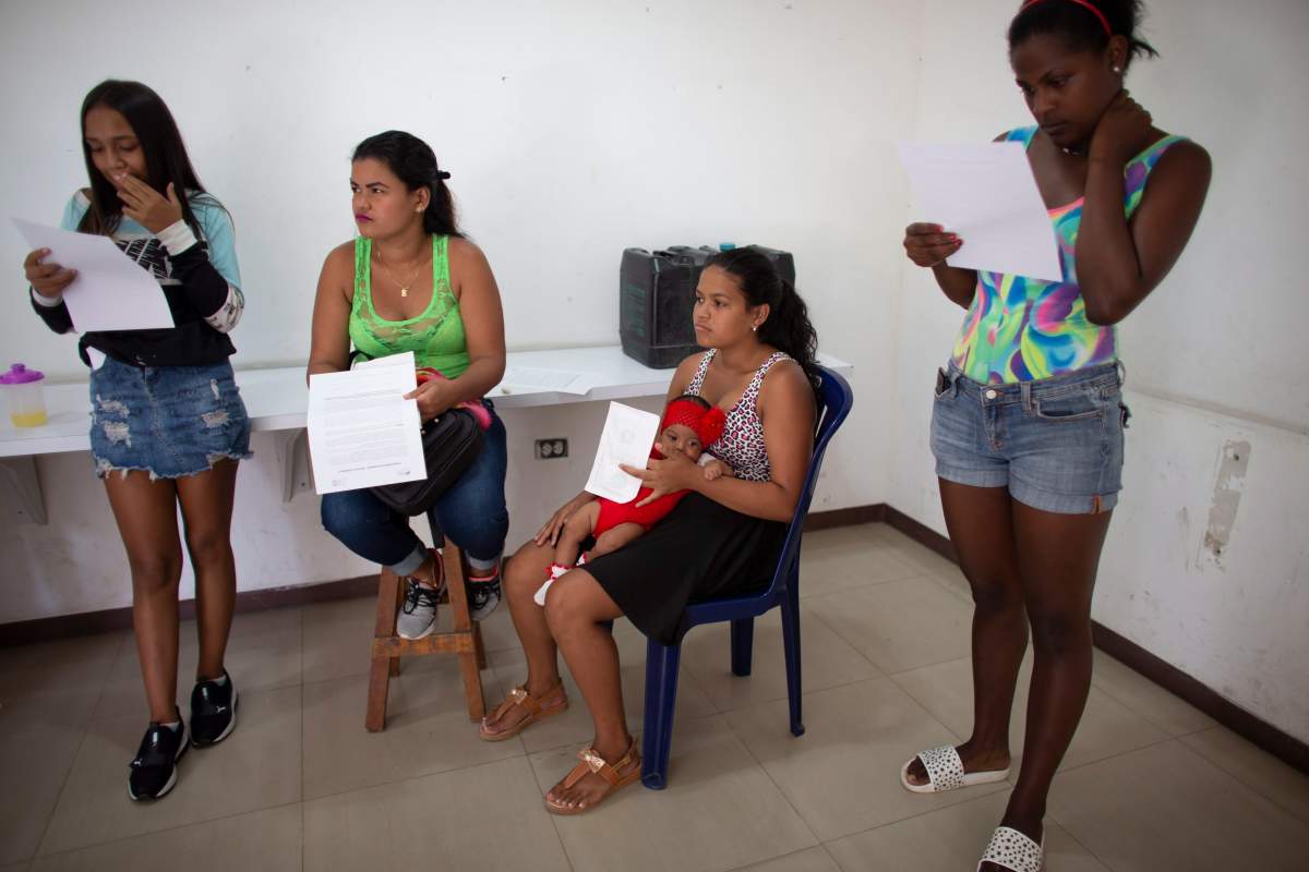 In this photo taken July 25, 2019, Nicol Ramirez, 15, sits with her baby girl and other women with forms to sign that authorizes the administration of hormonal implants to prevent pregnancies, of which there are a very limited number, in the Caucaguita neighborhood on the outskirts of Caracas, Venezuela.
