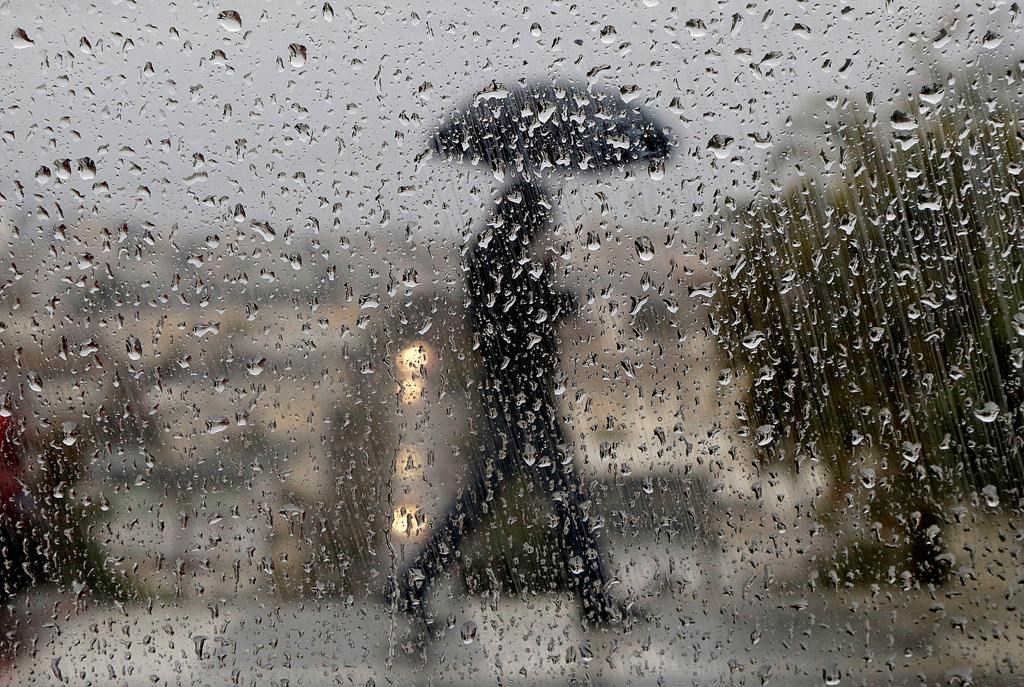 File: The silhouette of a person walking with an umbrella on a rainy day.