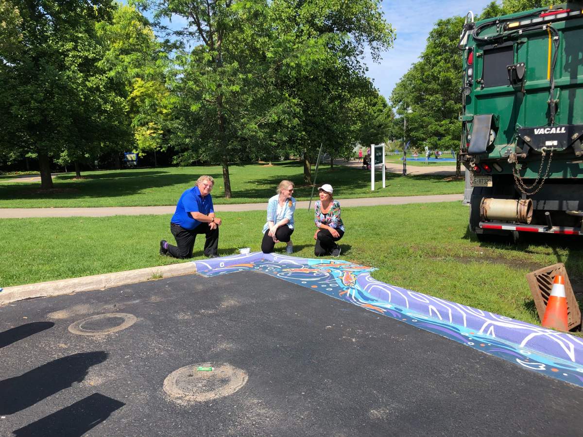 Erica Dornbusch, middle, kneels alongside Mayor Ed Holder and Ward 9 Coun. Anna Hopkins in front of her catchbasin artwork in Ivey Park.